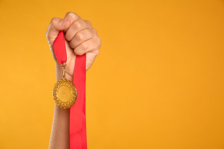 Woman holding gold medal on yellow background, closeup. Space for textの写真素材