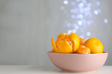 Tangerines in bowl on table against blurred lights, space for textの写真素材