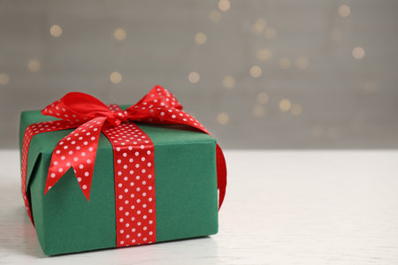 Beautifully wrapped gift box on white wooden table against blurred festive lights, space for textの写真素材