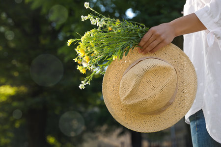 Young woman with straw hat and bouquet outdoors on sunny day, closeupの写真素材