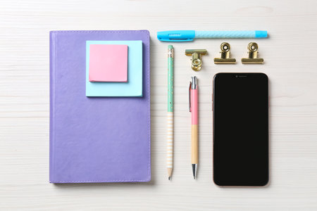 Flat lay composition with smartphone and stationery on white wooden tableの写真素材