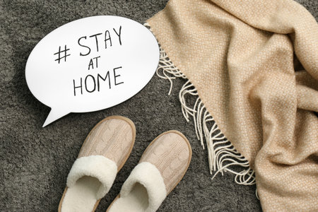 Slippers, plaid and speech bubble with hashtag STAY AT HOME on gray carpet, flat lay. Message to promote self-isolation during COVID?19 pandemicの写真素材