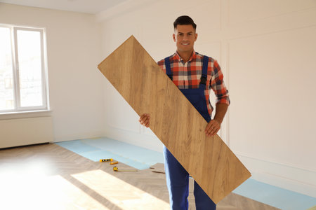 Professional worker with wooden board indoors. Installation of parquet flooringの写真素材