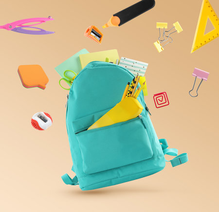 Backpack surrounded by flying school stationery on pale orange backgroundの写真素材