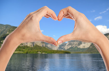 Woman making heart with hands near river and mountains on sunny day, closeupの写真素材