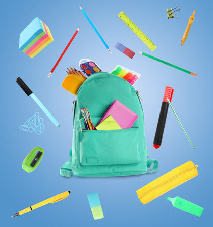 Backpack surrounded by flying school stationery on light blue backgroundの写真素材