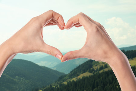 Woman making heart with hands in mountains on sunny day, closeupの写真素材