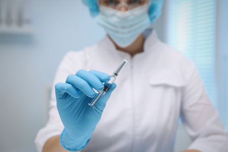 Doctor holding syringe with COVID-19 vaccine on blurred background, closeupの写真素材