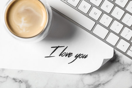 Card with text I Love You, cup of coffee and keyboard on white marble table, flat layの写真素材