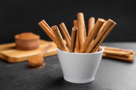 Aromatic cinnamon sticks in bowl on black tableの写真素材