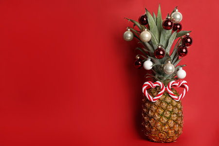 Pineapple with party glasses and Christmas tree balls on red background, space for text. creative conceptの写真素材