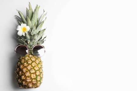 Pineapple with sunglasses and plumeria flower on white background, top view. creative conceptの写真素材