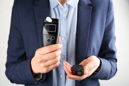 Woman holding modern breathalyser and car key on light background, closeupの写真素材