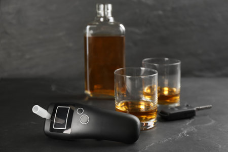 Modern breathalyser , car key and alcohol on black tableの写真素材