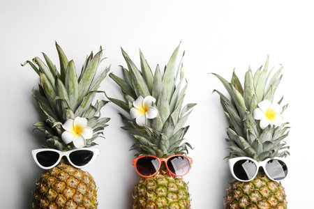 Pineapples with sunglasses and plumeria flowers on white background, top view. creative conceptの写真素材
