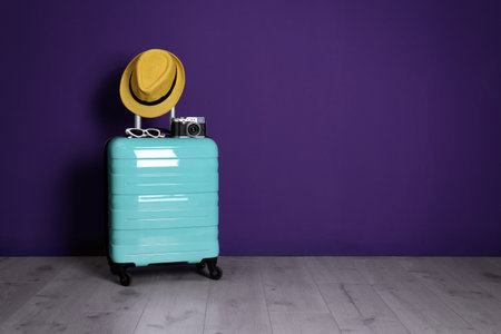 Travel suitcase with hat, camera and sunglasses on wooden floor near purple wall, space for text. summer holidaysの写真素材