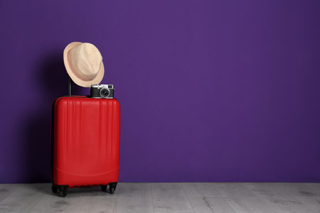 Travel suitcase with hat and camera on wooden floor near purple wall, space for text. summer holidaysの写真素材