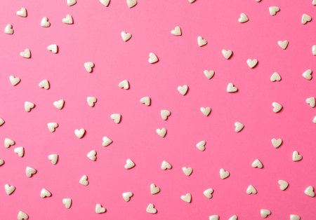 White heart shaped sprinkles on pink background, flat layの写真素材