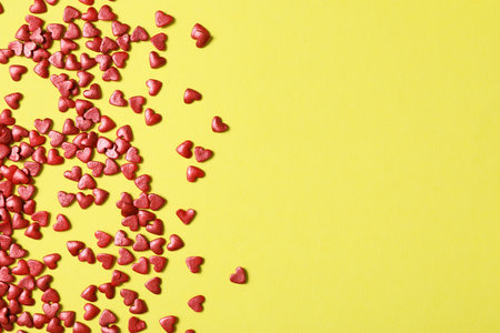 Bright heart shaped sprinkles on yellow background, flat lay. Space for textの写真素材