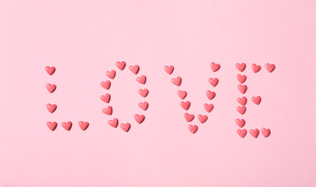 Word Love made with heart shaped sprinkles on pink background, flat layの写真素材