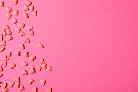 Heart shaped sprinkles on pink background, flat lay. Space for text