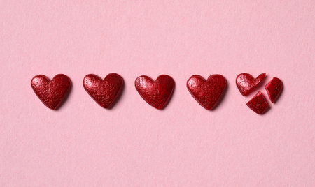 Red heart shaped sprinkles and one broken on pink background, flat lay