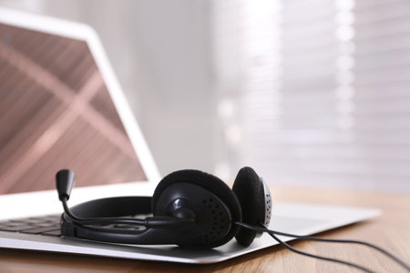 Modern laptop with headset on wooden table in office, space for text. hotline serviceの写真素材