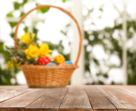 Empty wooden surface and wicker basket with colorful Easter eggs on backgroundの写真素材