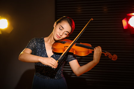 Beautiful young woman playing violin in dark roomの写真素材
