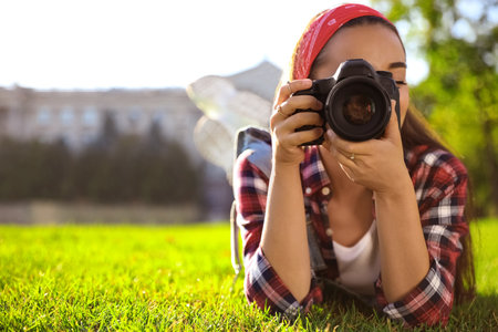 Young photographer taking picture with professional camera on green grass. Space for textの写真素材