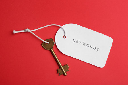 Metal key and tag wIth word KEYWORDS on red background, top viewの写真素材