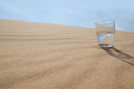 Glass of water on sand in desert. Space for textの写真素材