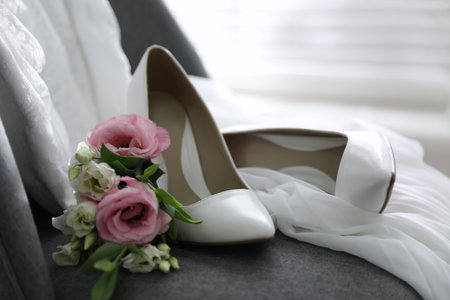 Pair of white high heel shoes, flowers and wedding dress on chair indoorsの写真素材