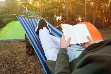 Man with book resting in comfortable hammock outdoors, closeupの写真素材
