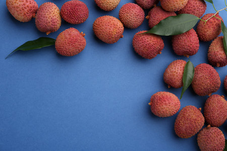 Fresh ripe lychees with leaves on blue background, flat lay. Space for textの写真素材