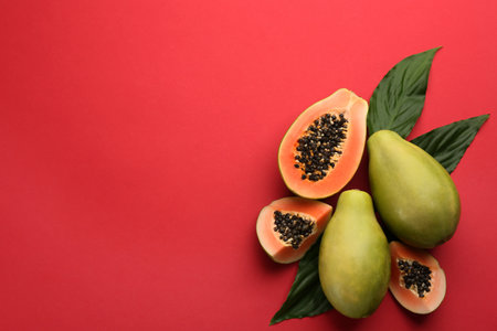 Fresh ripe papaya fruits with green leaves on red background, flat lay. Space for textの写真素材