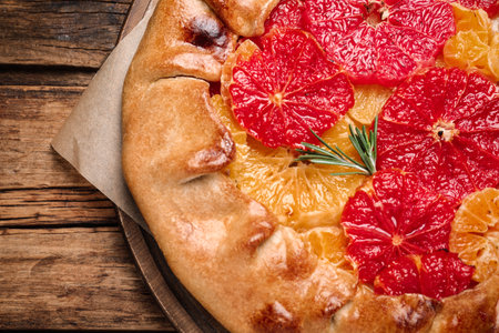 Tasty galette with citrus fruits and rosemary on wooden table, top viewの写真素材