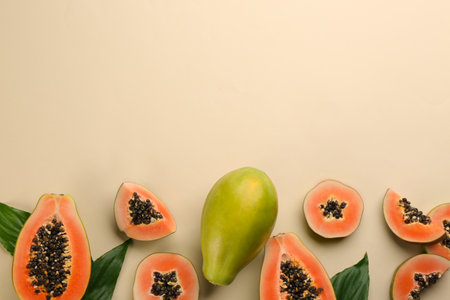 Fresh ripe papaya fruits with green leaves on beige background, flat lay. Space for textの写真素材