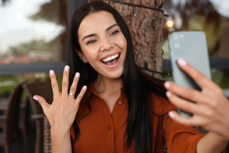 Happy woman with engagement ring taking selfie in outdoor cafeの写真素材