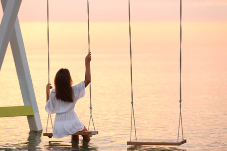 Young woman enjoying sunrise on swing over waterの写真素材