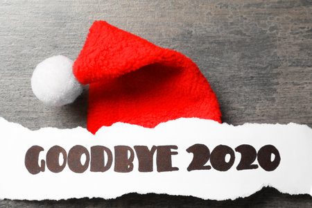 Paper sheet with text Goodbye 2020 and Santa hat on gray background, flat layの写真素材