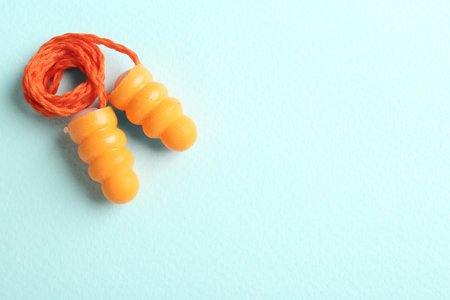 Pair of orange ear plugs with cord on turquoise background, top view. Space for textの写真素材