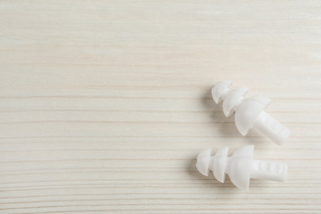 Pair of ear plugs on white wooden background, flat lay. Space for text