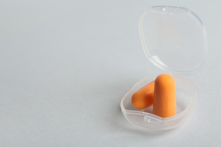 Pair of orange ear plugs in case on white background. Space for textの写真素材