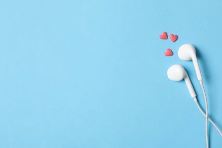 Modern earphones and pink heart shaped sprinkles on light blue background, flat lay with space for text. Listening love music songsの写真素材