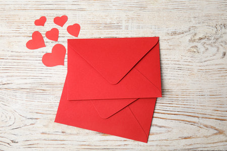 Red envelopes and paper hearts on white wooden table, flat lay. love letters