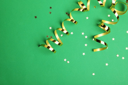 Shiny golden serpentine streamers and confetti on green background, flat lay. Space for textの写真素材
