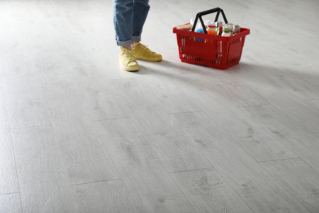 Woman and shopping basket with groceries on white wooden floor, closeup. Space for text