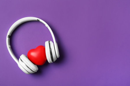 Modern headphones and red heart on purple background, flat lay with space for text. Listening love music songsの写真素材