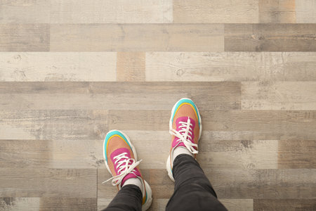 Woman in colorful sneakers standing on wooden floor, top view. Space for textの写真素材